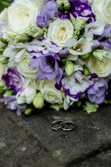 Wedding rings resting on stone with bridal bouquet in background