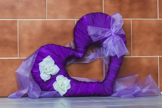 Purple heart decoration with white flowers leaning against a tiled wall