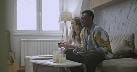 A young couple enjoys playing video games together in their cozy living room, sharing laughter and friendly competition. - Powered by Adobe