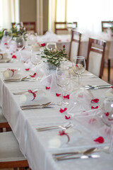 Wedding table setting decorated with red rose petals and greenery