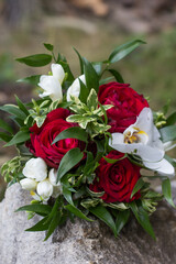Wedding bouquet combining red roses, white freesia and orchid flowers resting on a rock
