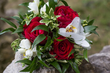 Wedding bouquet combining red roses, white freesia and orchid flowers resting on a rock