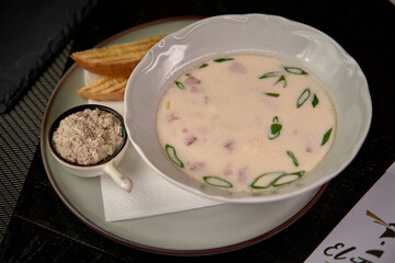 A bowl of creamy soup garnished with green onions served alongside a side of toasted bread and a small dish of savory spread, perfect for a delightful meal experience.