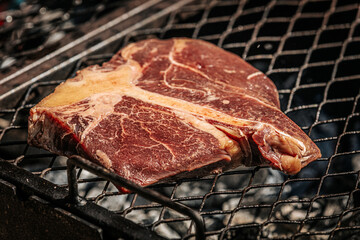 A thick-cut raw tomahawk steak rests on a hot metal grill, showcasing rich marbling and a long bone handle. Ideal for barbecue or steakhouse-style cooking.