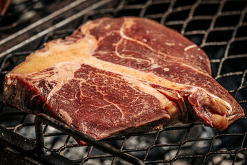 A thick-cut raw tomahawk steak rests on a hot metal grill, showcasing rich marbling and a long bone handle. Ideal for barbecue or steakhouse-style cooking.