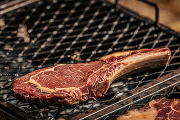 A thick-cut raw tomahawk steak rests on a hot metal grill, showcasing rich marbling and a long bone handle. Ideal for barbecue or steakhouse-style cooking.