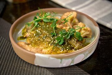 A beautifully plated dish of fish topped with green sauce, garnished with fresh microgreens, served alongside roasted cauliflower, creating an appetizing culinary experience.