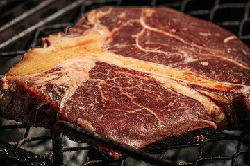 A thick-cut raw tomahawk steak rests on a hot metal grill, showcasing rich marbling and a long bone handle. Ideal for barbecue or steakhouse-style cooking.