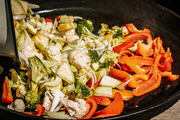 Colorful medley of steaming stir-fried vegetables including cauliflower, bell peppers, broccoli, onions, and zucchini, being cooked in a hot pan.