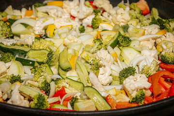 Colorful medley of steaming stir-fried vegetables including cauliflower, bell peppers, broccoli, onions, and zucchini, being cooked in a hot pan.