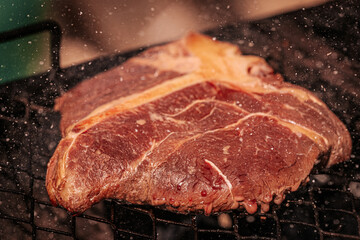 Close-up of a thick raw T-bone steak sizzling on a grill with visible marbling and seasoning...