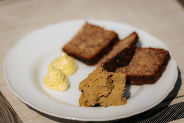 Plate with three slices of dark rye bread, a serving of liver pâté, and two decorative swirls of butter on a white dish atop a beige placemat.