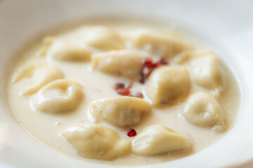Creamy dumplings in a rich sauce garnished with red peppercorns, served in a white bowl. Soft texture and subtle spices give it a gourmet look.