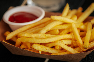 A close-up of a juicy cheeseburger with lettuce and sauce, served alongside golden French fries and a cup of ketchup on a rustic wooden tray.