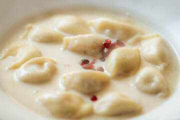 Creamy dumplings in a rich sauce garnished with red peppercorns, served in a white bowl. Soft texture and subtle spices give it a gourmet look.