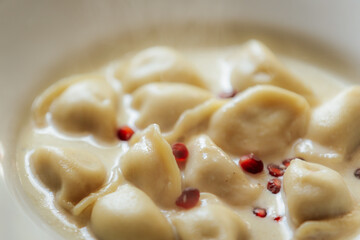 Creamy dumplings in a rich sauce garnished with red peppercorns, served in a white bowl. Soft texture and subtle spices give it a gourmet look.