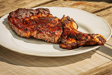 Close-up of a juicy grilled T-bone steak on a white plate, being sliced with a fork and knife. Cooked to perfection with visible grill marks and seared crust.