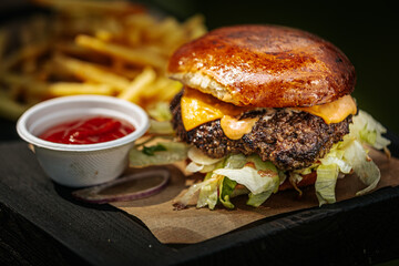 A close-up of a juicy cheeseburger with lettuce and sauce, served alongside golden French fries and a cup of ketchup on a rustic wooden tray.