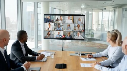 Professionals participate in a video conference in a modern office boardroom showing a diverse grid of remote participants on a large screen - Powered by Adobe