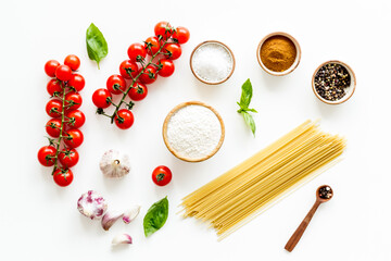 Spaghetti with ingredients for cooking Italian pasta - tomatoes and basil with garlic - on a white background, top view. Flat lay