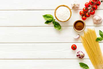 Flat lay of uncooked spaghetti with ingredients for cooking Italian pasta - tomatoes and basil with garlic - on a white wooden background, top view