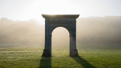 Fototapeta premium Ancient stone archway in a misty field at sunrise with sunbeams