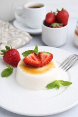 Tasty panna cotta with caramel, strawberries, mint and coffee on table, closeup