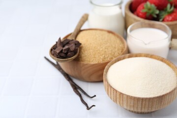 Different ingredients for panna cotta. Milk, sugar, vanilla, chocolate and strawberries on white tiled table, closeup. Space for text