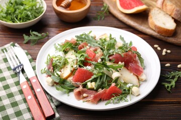 Tasty salad with arugula, prosciutto, cheese, pear, grapefruit and nuts on wooden table, closeup