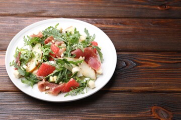 Tasty salad with arugula, prosciutto, cheese, pear, grapefruit and nuts on wooden table, closeup. Space for text