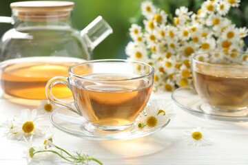 Aromatic tea in glass cups and chamomile flowers on white wooden table, closeup