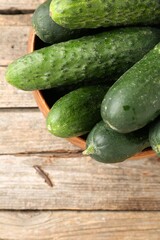 Fresh cucumbers in bowl on wooden table, top view