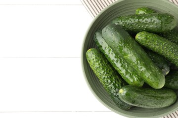 Fresh cucumbers in bowl on white wooden table, top view. Space for text
