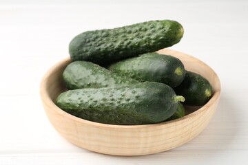 Fresh cucumbers in bowl on white wooden table, closeup