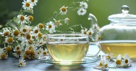 Tasty chamomile tea and flowers on grey table, closeup