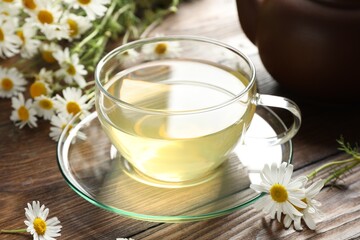 Tasty chamomile tea and flowers on wooden table, closeup