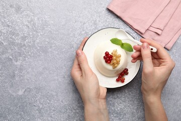 Woman eating tasty panna cotta with currants and mint at light grey table, top view. Space for text
