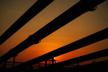 Silhouetted Industrial Pipes Against Orange Sunset Sky pipeline