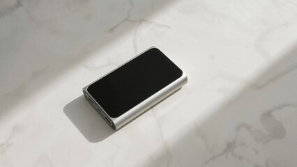 Silver Portable Power Bank with Black Screen on Marble Surface with Sunlight Shadows