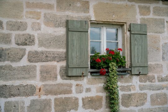 Rustikales Fenster mit roten Geranien und gr&uuml;nen Holzl&auml;den