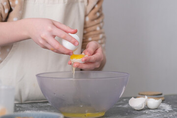 Young child focuses on cracking eggs into a mixing bowl, surrounded by baking tools and ingredients on a kitchen countertop. A warm atmosphere fills the space.