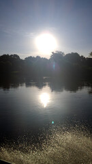 Fototapeta premium Serene sunset over Cuiaba River in the Pantanal wetlands, with sun reflecting on the water surface and silhouetting the dense forest trees. Water splashes in the foreground create a beautiful sparkle.