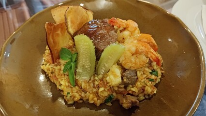 Exquisite surf and turf risotto with tender beef filet and grilled shrimp, elegantly garnished with fresh basil, cucumber slices, and crispy sweet potato chips, served in a ceramic bowl.