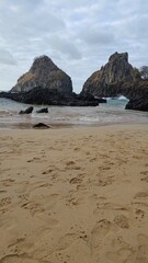 Scenic view of Pigs Bay (Baia dos Porcos) with golden sand and footprints, facing Two Brothers Hill (Morro Dois Irmãos) in the ocean. Fernando de Noronha, a beautiful, remote, and natural destination.
