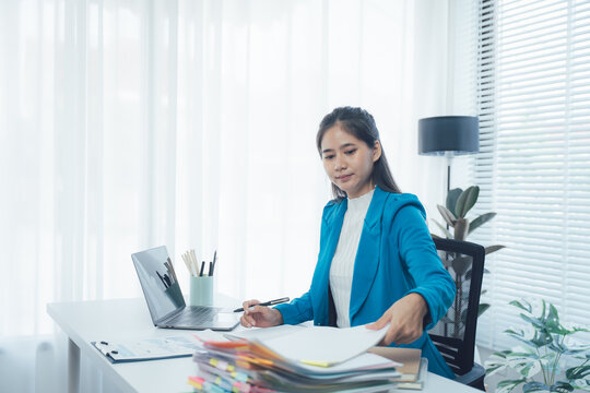 Focused at Work: A dedicated woman is fully engrossed in her work, meticulously reviewing documents, using a laptop, and ensuring attention to detail in a well-lit, organized workspace.