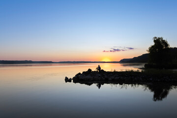 silhouette of a man contemplative at sunset on a rock ledge