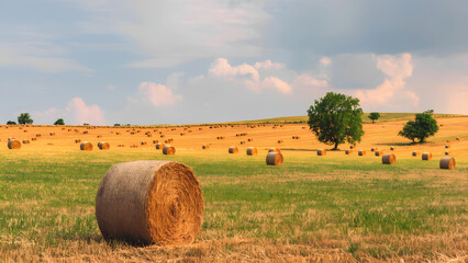 A vast rural landscape featuring a large, rectangular bale of hay in the foreground. The hay bale is golden brown and neatly stacked.