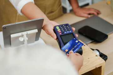closeup view customer tapping credit card on payment terminal in flower shop with wooden counter...