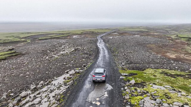 Silver SUV embarking on an Icelandic adventure on a gravel road full of potholes on a rainy day