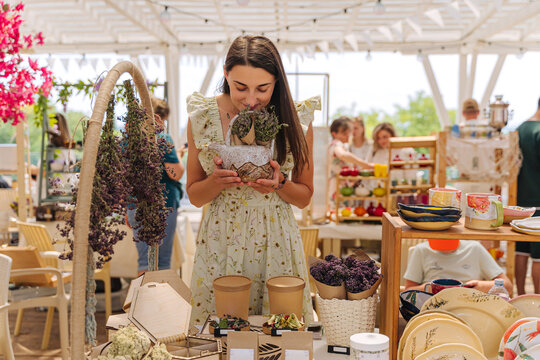 Female Artisan Selling Dried Flowers, Herbal Teas, and Handmade Ceramics at Summer Outdoor Craft Market